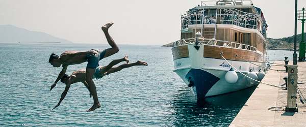 Tuffo di due turisti dal molo nel mare cristallino, Golfo del Quarnaro, Croazia.