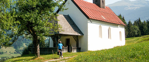 Piccola chiesa con tetto rosso immersa nel verde tra le montagne lungo la Ciclabile della Drava, Austria