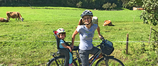 Famiglia in bicicletta attraverso i prati verdi di Villach, Carinzia, tra mucche al pascolo nei prati e boschi