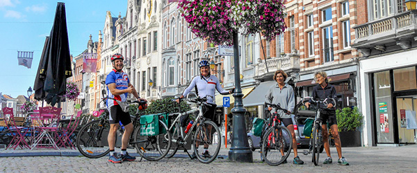 Strada pedonale con edifici storici e fiori appesi nelle Fiandre. viaggi in gruppo con Girolibero.