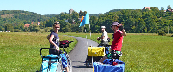 Genitori in bici con carrellino per bambini nei paesaggi verdi della Baviera.