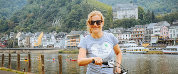 Cicloturista in viaggio con Girolibero sorridente e con occhiali da sole lungo ciclabile della Mosella, castello imperiale di Cochem, Germania
