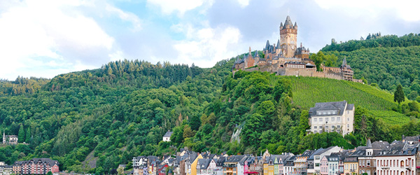 Blick auf die Mosel und die Reichsburg Cochem mit bunten Häusern am Flussufer.