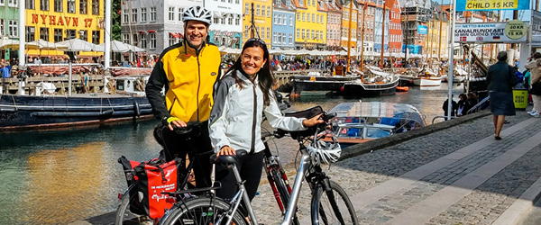 Coppia di ciclisti sorridenti nel quartiere di Nyhavn con le sue case colorate lungo il canale, Copenaghen, Danimarca