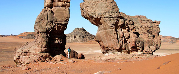 Formazione rocciosa naturale ad arco nel deserto del Sahara, circondata da paesaggi aridi e cielo limpido.
