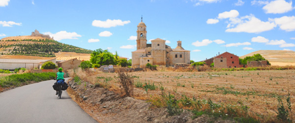 Ciclista lungo una strada nel percorso per Santiago con un monastero medioevale sullo sfondo