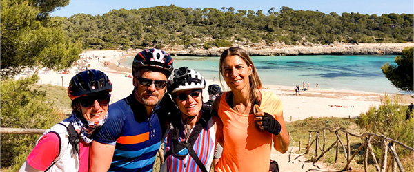 Gruppo di amici sorridenti con il mare sullo sfondo a Maiorca, vacanze in bici 