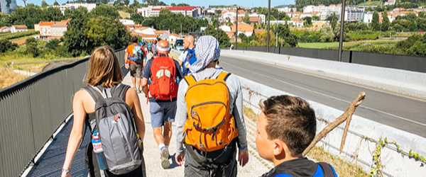 Gruppo di pellegrini con zaini che percorrono un sentiero assolato sul Cammino di Santiago.