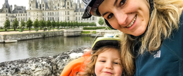 Ciclista sorridente con bambina su bici lungo il fiume Loira, di fronte al castello di Amboise, viaggiare in bici in famiglia