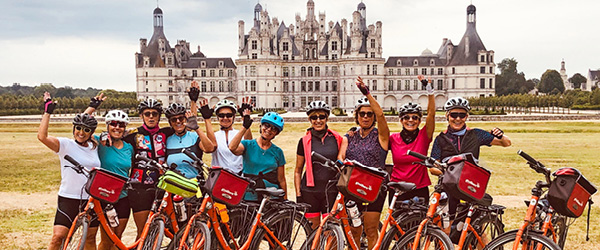 Gruppo di ciclisti davanti a un castello storico europeo nella valle della Loira, tappa culturale durante un itinerario in bicicletta.