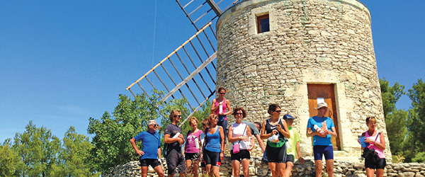 Gruppo davanti a un mulino a vento storico in un paesaggio collinare durante un viaggio in Provenza.