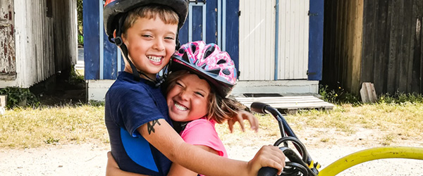 Bambini si abbracciano felici su una bicicletta, Francia in bici in famiglia