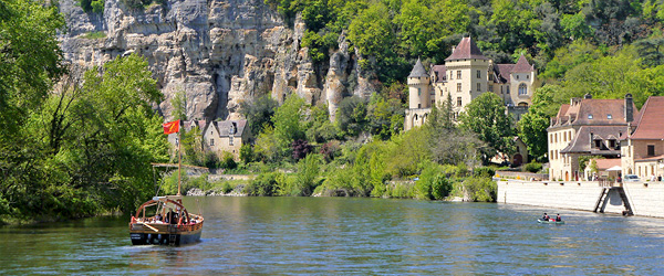 Barca sul fiume Dordogna che passa davanti al villaggio di La Roque-Gageac circondato da colline verdi, Francia