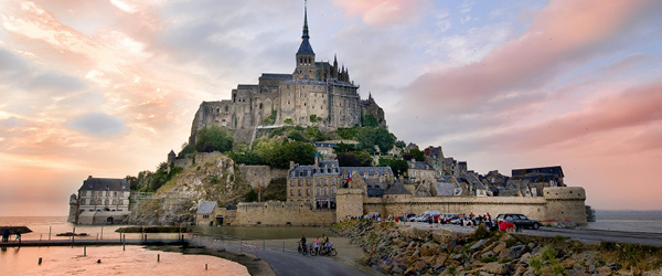 Veduta di Mont Saint-Michel, Normandia e Bretagna, Francia, con pontile e ciclisti lungo la strada d'accesso.