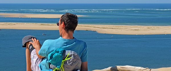 Viaggiatore con zaino seduto su una duna di sabbia con vista sulla baia di Arcachon