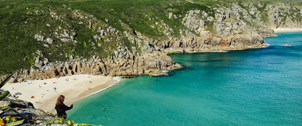 Viaggiatrice ammira il panorama su una baia con acqua turchese e scogliere verdi in Cornovaglia, Regno Unito.