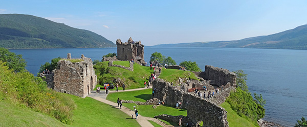 Veduta del castello di Urquhart sul lago di Loch Ness lungo il percorso del Great Glen Way, circondato da colline verdi e visitatori sul prato, Scozia.