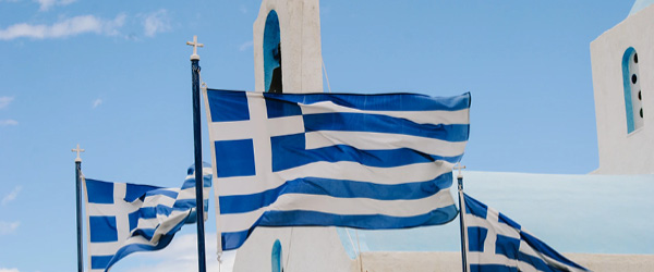 Bandiere greche sventolano davanti a una chiesa bianca sull'isola di Santorini, Grecia.