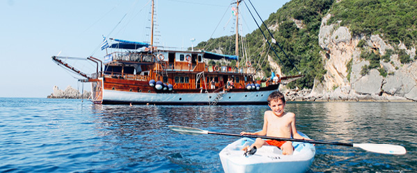 Bambino sorridente su una canoa, barca a vela sul mare blu con colline verdi sullo sfondo, viaggi in barca 