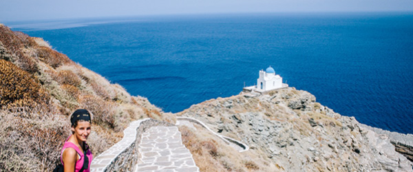 Escursionista su un sentiero con vista sul mare e cappella di Profitis Ilias, Grecia