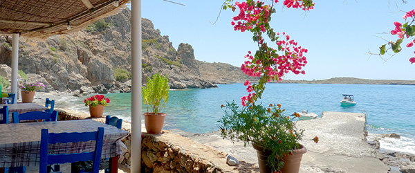 Taverna tradizionale sul mare a Loutro, Creta, Grecia, con tavoli all’ombra e vista panoramica.