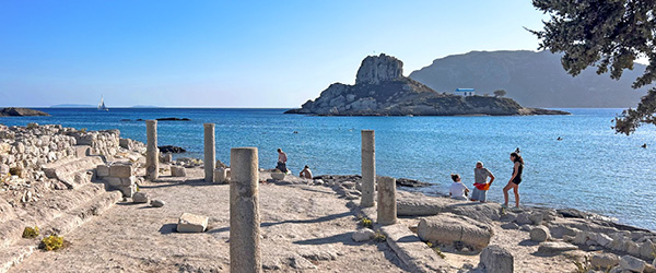 Rovine antiche sulla spiaggia di Kos con colonne e visitatori in esplorazione.