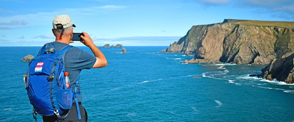 Escursionista scatta una foto su una scogliera con vista panoramica sull'oceano lungo il Wild Atlantic Way.