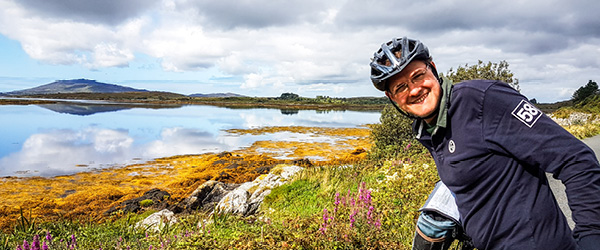 Ciclista sorridente su un sentiero panoramico tra le colline del Connemara, Irlanda, con vista sulle montagne.