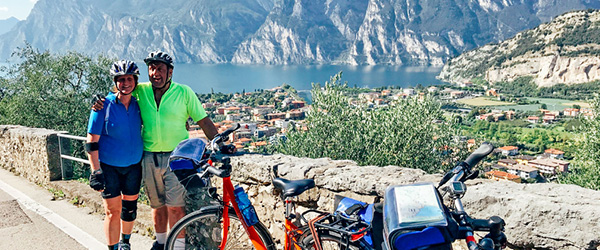 Coppia di cicloturisti in posa per una foto con lago e montagne, biciclette arancioni 