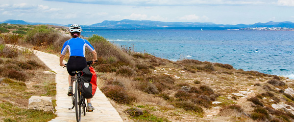 Ciclista pedala su un sentiero lungo la costa, vacanze in bici in Sardegna