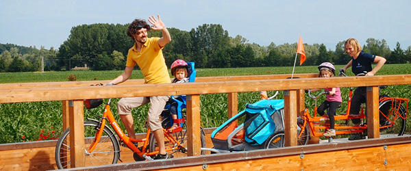 Menschen überqueren eine Holzbrücke mit Weinbergen im Hintergrund, Euganeische Hügel, Familienradurlaub