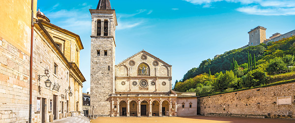 Vista della Piazza del Duomo a Spoleto con la Cattedrale di Santa Maria Assunta e il cielo blu sullo sfondo.