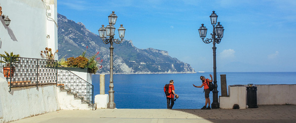 Escursionista sul lato un edificio bianco con piante e scalini con corrimano, mare limpido sullo sfondo, Costiera Amalfitana