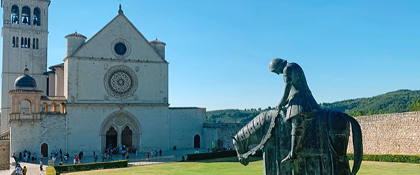 Basilica of Saint Francis in Assisi with equestrian statue and blue sky.