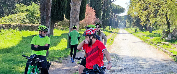 Radfahrer auf Reisen mit Girolibero auf der Via Appia Antica in Rom, Italien – Radfahrer genießen eine Tour entlang der historischen Via Appia Antica, umgeben von Zypressen und römischen Ruinen.