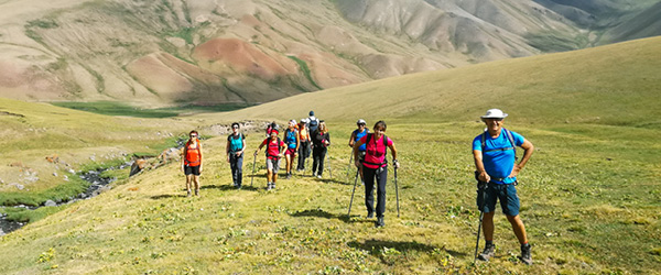 Gruppo di escursionisti in vacanza con Girolibero cammina su una verde vallata con montagne innevate sullo sfondo in Kirghizistan. La terra delle aquile: tra natura mozzafiato e tradizioni millenarie Fabio Bianchi