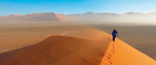 Escursionista che cammina sulla cresta di una duna di sabbia nel deserto della Namibia, viaggiare con 