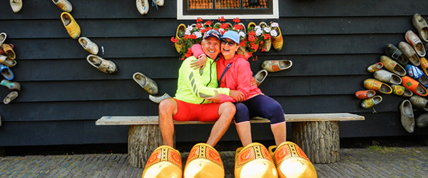 Zwei Personen sitzen auf großen Holzschuhen vor einem traditionellen niederländischen Geschäft.