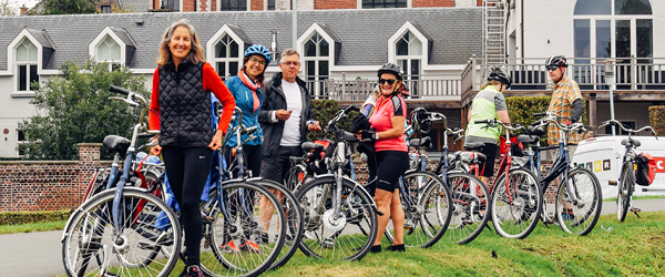 Gruppo di turisti in bicicletta lungo un canale circondato da alberi e case tipiche
