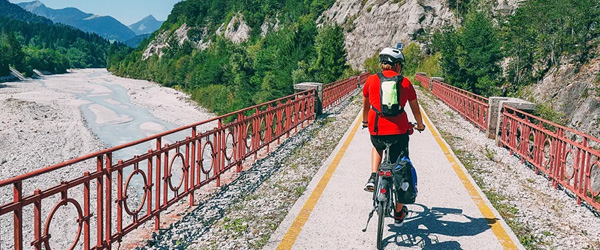 Ciclista che attraversa il ponte rosso sulla Ciclovia Alpe Adria Radweg vicino a Tarvisio nelle Alpi Friulane