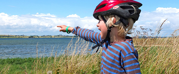 Bambina con casco che indica il mare da una collina erbosa, isola di Fyn