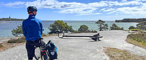 Ciclista con bici da viaggio lungo una strada costiera della Svezia, paesaggio nordico e mare.