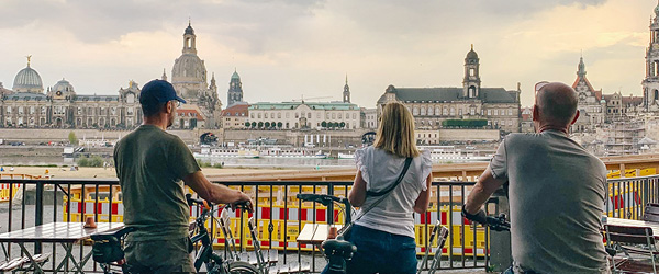 Tre cicloturisti girati di spalle osservano la città sul fiume Elba al tramonto