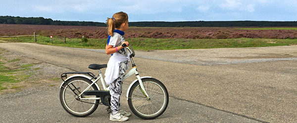 Bambina in bicicletta su strada di campagna nei Paesi Bassi, cicloturismo family-friendly tra paesaggi rurali olandesi.