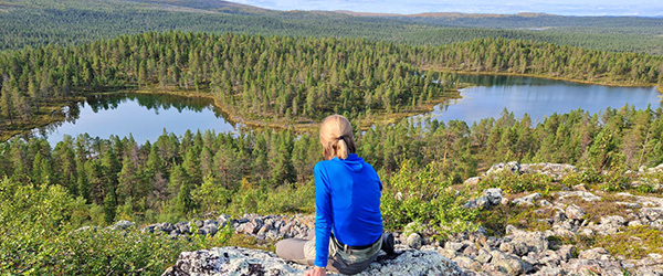 Viaggiatore su roccia panoramica tra laghi e foreste della Finlandia, paesaggio naturale tipico della regione dei laghi