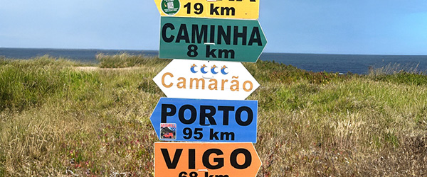 Segnavia colorato del Cammino di Santiago con indicazioni verso Santiago de Compostela, Porto e Vigo, lungo un tratto rurale della Galizia