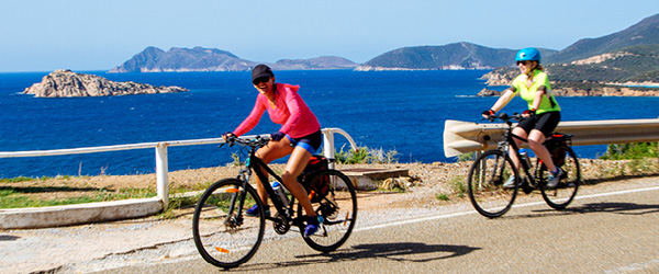 Gruppo di ciclisti su una strada costiera in Sardegna con vista sul mare