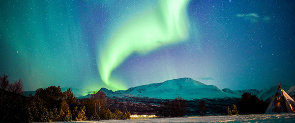 Aurora boreale verde e viola nel cielo stellato sopra un paesaggio montuoso innevato della Norvegia settentrionale.