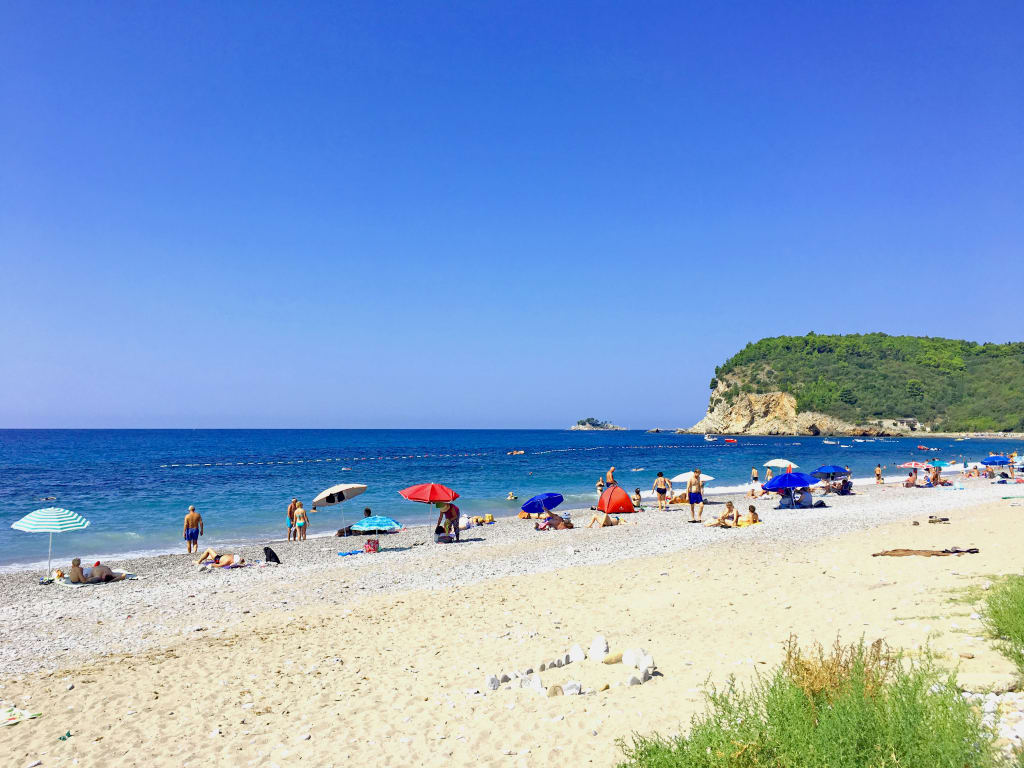 Spiaggia sabbiosa con acque cristalline e colline sullo sfondo in Albania.