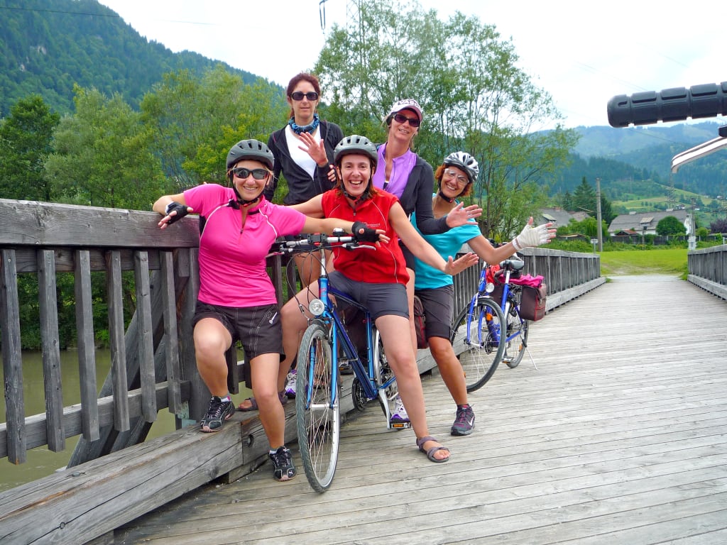 Famiglia felice in posa con le bici su un ponte con vista sulle montagne lungo la Ciclabile dei Tauri.